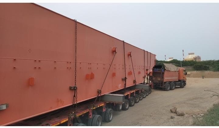 A large fabricated steel module chained across multi-axle trailer lines on a site approach road